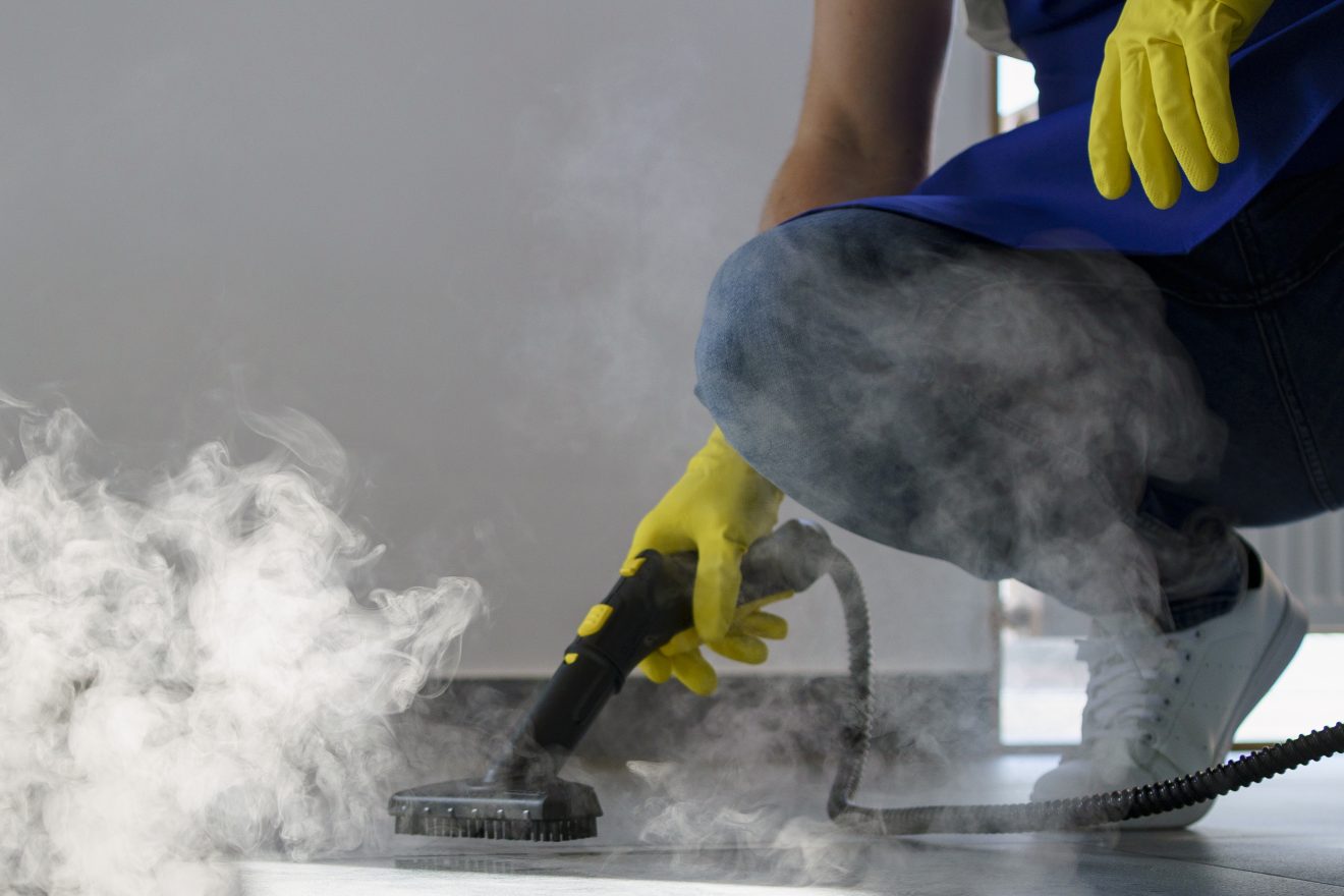 Professional cleaner in blue apron and yellow gloves using a steam cleaner on a hard floor