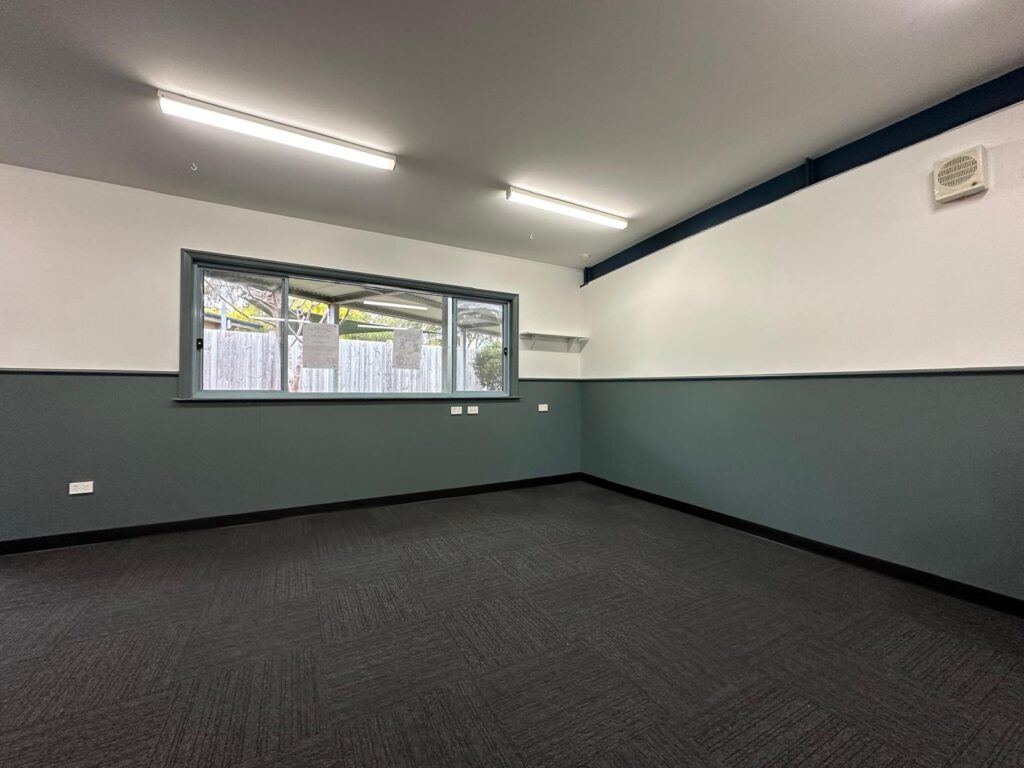 Restored classroom corner with new dark carpet, cleaned walls and window ready for reinstatement