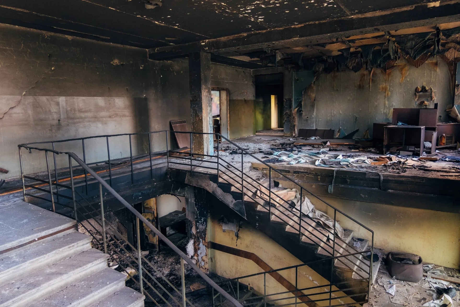Severely fire-damaged building interior with charred walls, debris, and collapsed staircase.