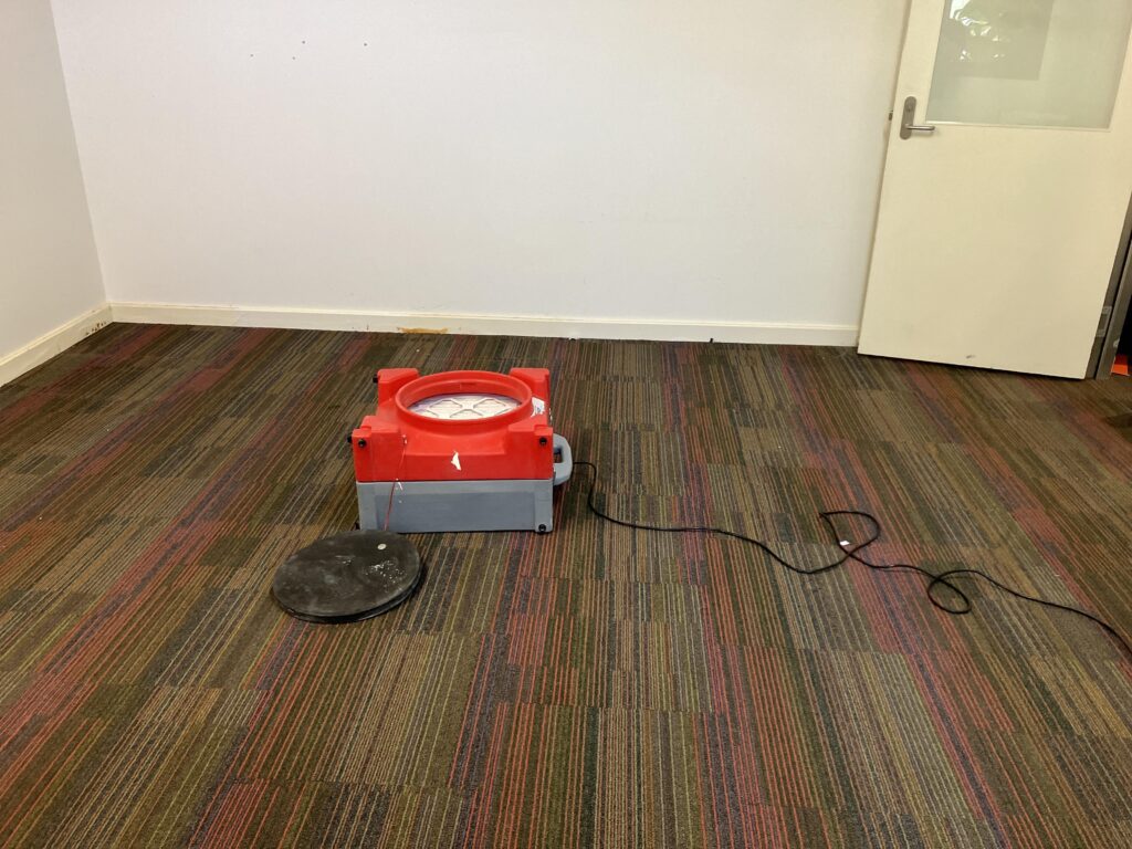 HEPA-filtered air scrubber operating on carpeted classroom floor under negative air pressure containment