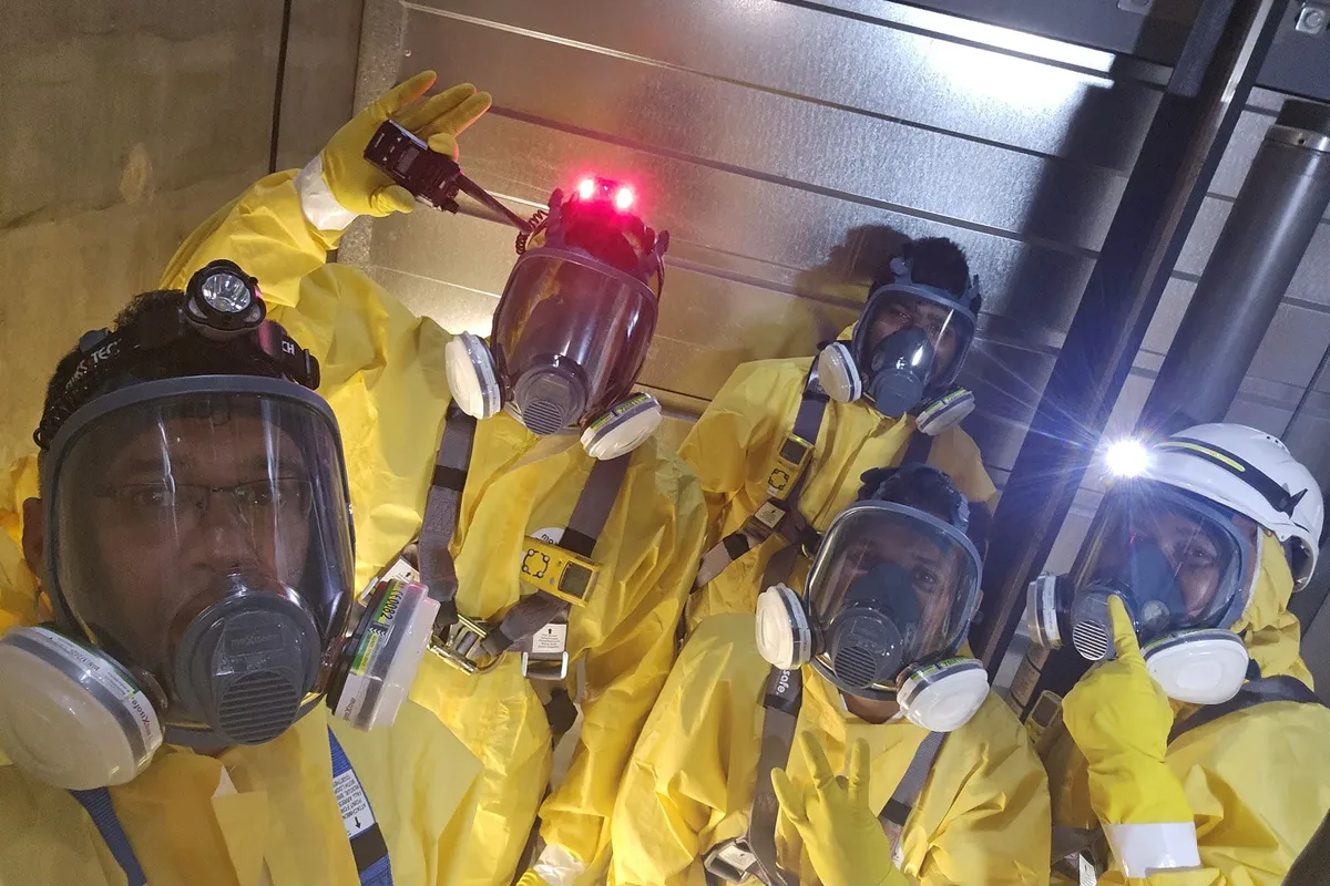 Confined space crew in full-face respirators and hazmat suits on site