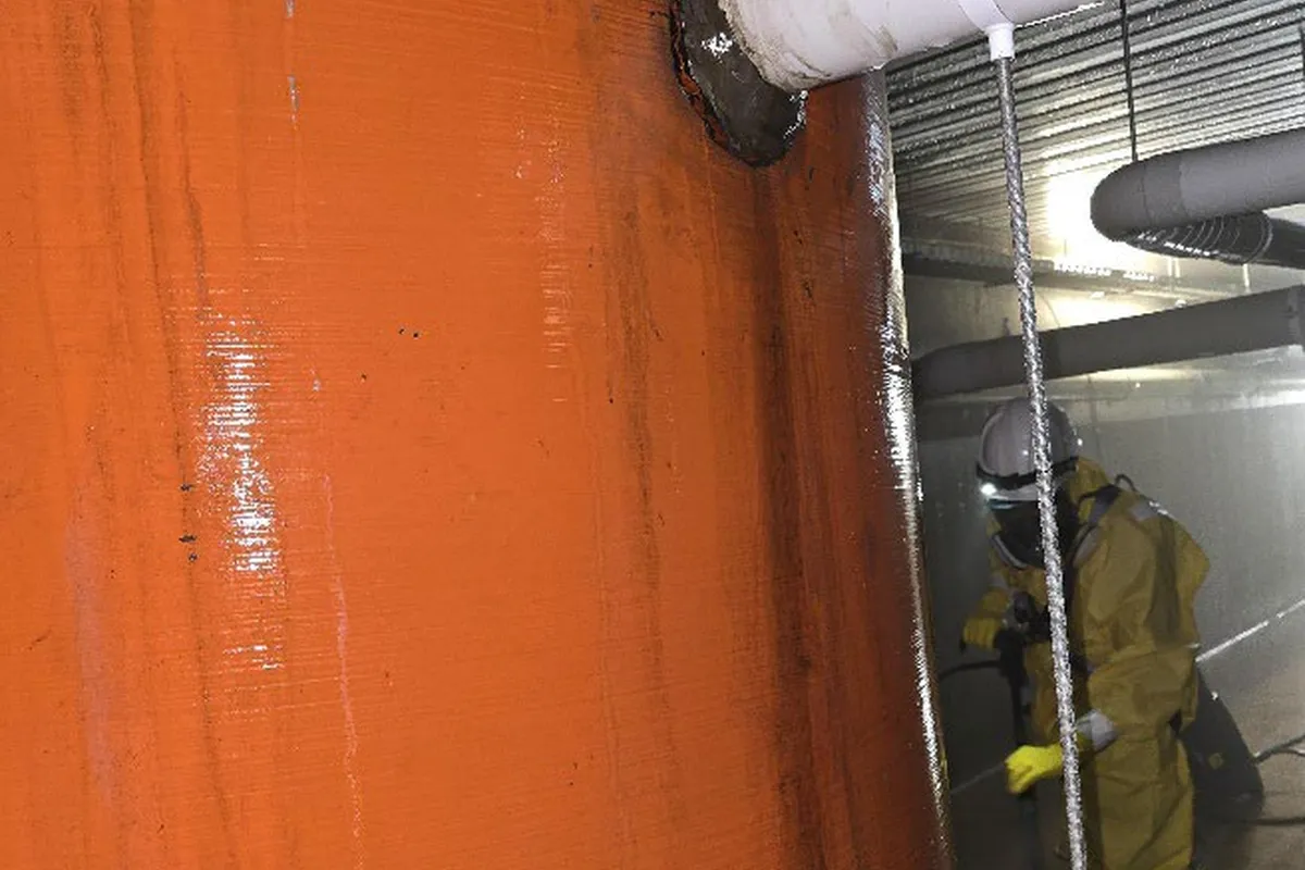 Worker in protective suit alongside industrial tank inside the plant room