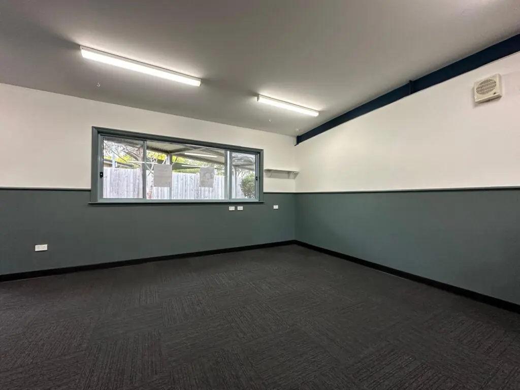 Restored classroom corner with new dark carpet, cleaned walls and window ready for reinstatement